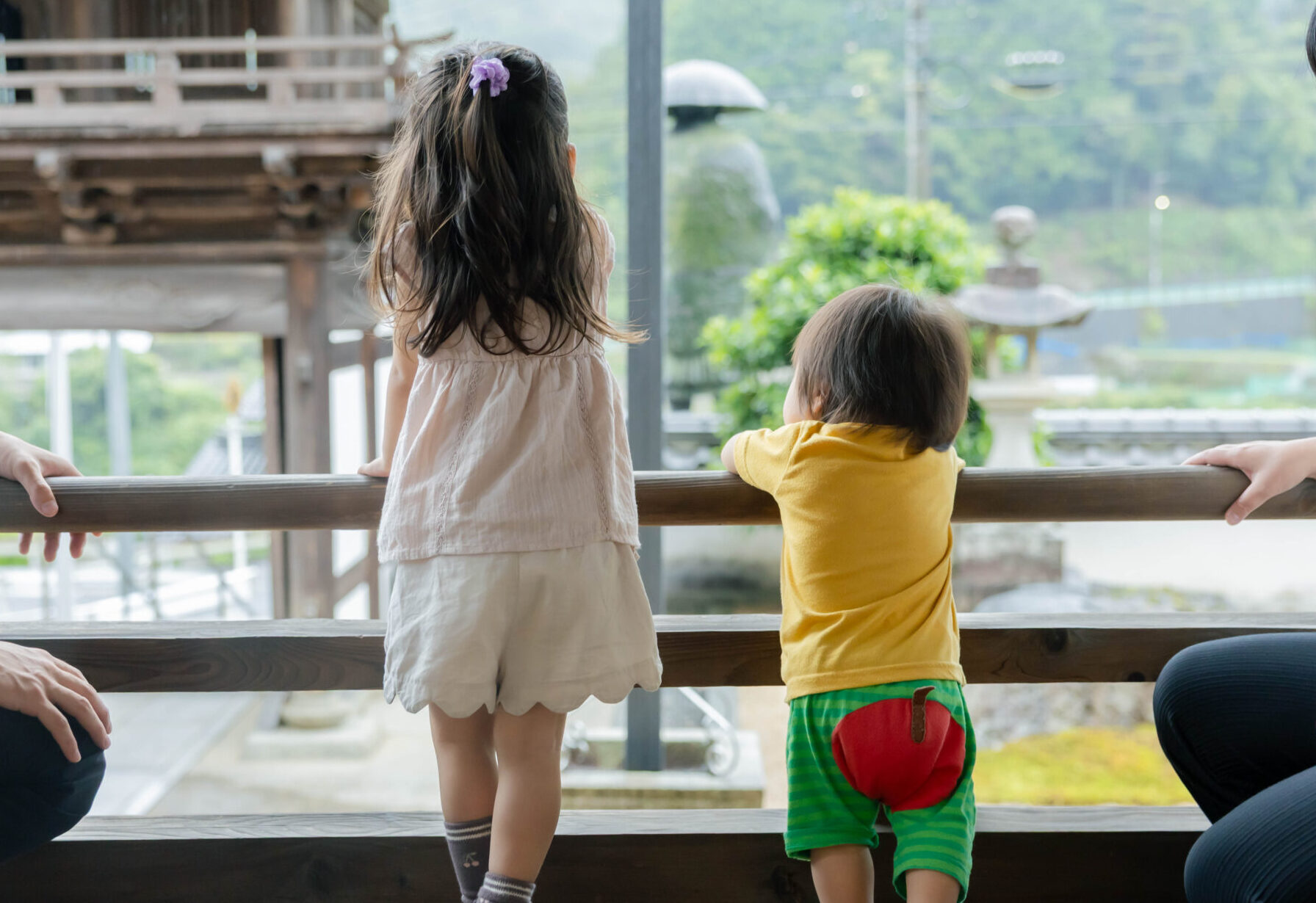 お寺の縁側から外をながめる子どもたちと、見守る大人